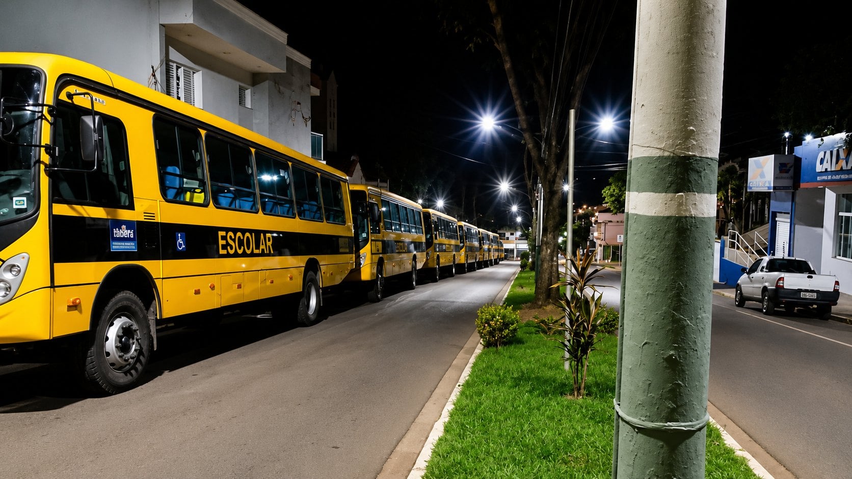 Fila de ônibus escolares amarelos estacionados em avenida de Itaberá à noite
